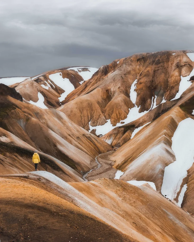 A girl in yellow jacket looking into the colorful mountains of Landmannalaugar in the highlands of Iceland