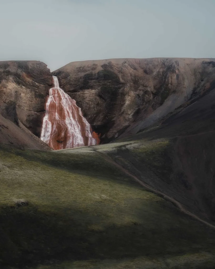 The red Raudufossar waterfall in the moss-green landscape of the highlands of Iceland