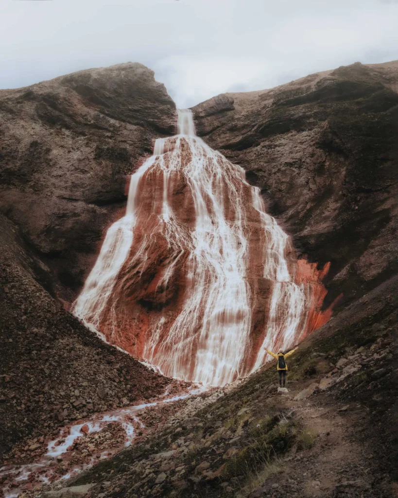 The red Raudufossar waterfall in the moss-green landscape of the highlands of Iceland